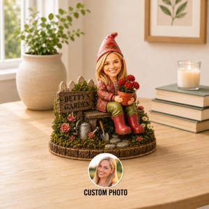 May include: A custom figurine featuring a smiling person with blonde hair wearing a red hat, a patterned jacket, green pants, and red boots. The figure sits on a bench next to a sign reading BETTY'S GARDEN, a small potted plant, and a watering can.