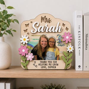 Könnte beinhalten: Ein Bilderrahmen aus Holz mit dem Text Mrs. Sarah oben und Thank you for helping me grow love, Sophia unten. Der Rahmen ist mit ausgeschnittenen Holzblumen in Rosa, Weiß und Grün sowie kleinen Schmetterlingsformen verziert.