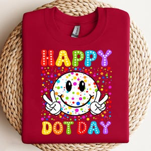 May include: A maroon sweatshirt with a colorful graphic. The graphic features a smiley face with peace signs and the words "HAPPY DOT DAY" in rainbow colors. The design is surrounded by colorful dots.