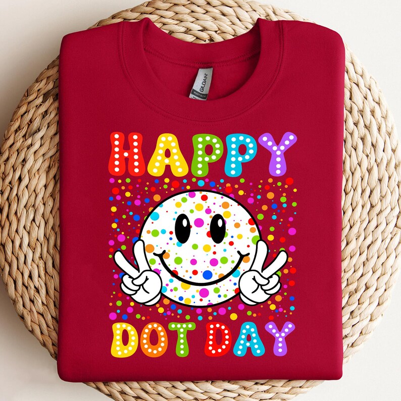 May include: A maroon sweatshirt with a colorful graphic. The graphic features a smiley face with peace signs and the words "HAPPY DOT DAY" in rainbow colors. The design is surrounded by colorful dots.