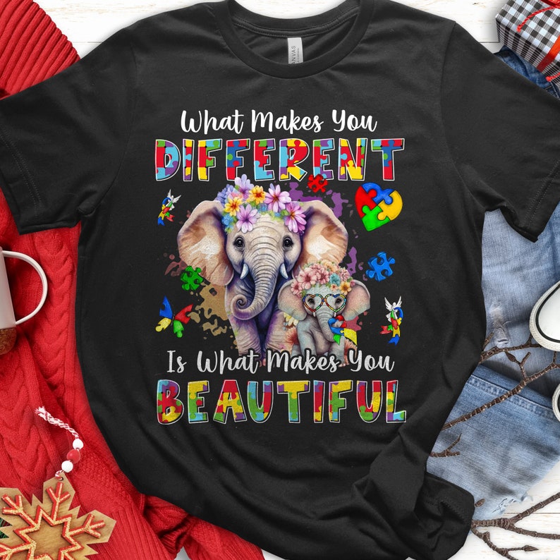 May include: Black t-shirt featuring a colourful puzzle piece design and two elephants. The text reads "What Makes You Different Is What Makes You Beautiful."