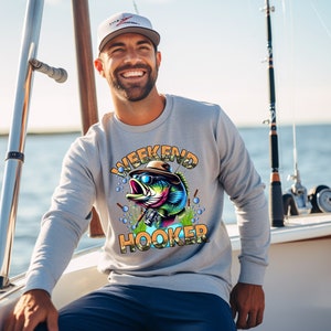 K&ouml;nnte beinhalten: Ein graues Sweatshirt mit einem bunten Cartoon-Fisch, der eine Sonnenbrille und einen Hut tr&auml;gt. Der Text "Weekend Hooker" ist auf dem Shirt aufgedruckt.