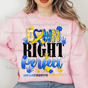 May include: Pink sweatshirt with a graphic design that says "Down Right Perfect" in black letters with a yellow and blue ribbon, blue puzzle pieces, and blue handprints. The text "#DownSyndromeAwareness" is at the bottom of the design.