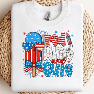 May include: White crew neck sweatshirt with a patriotic design. The graphic features a red, white, and blue popsicle wearing heart-shaped sunglasses, fireworks, and the words "Red, White, and Cute."