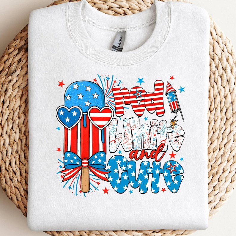 May include: White crew neck sweatshirt with a patriotic design. The graphic features a red, white, and blue popsicle wearing heart-shaped sunglasses, fireworks, and the words "Red, White, and Cute."
