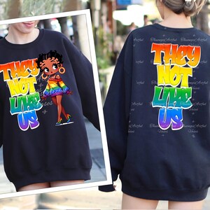 May include: Black sweatshirt with a rainbow graphic that says "They Not Like Us" and a cartoon image of a woman with a rainbow sweater.