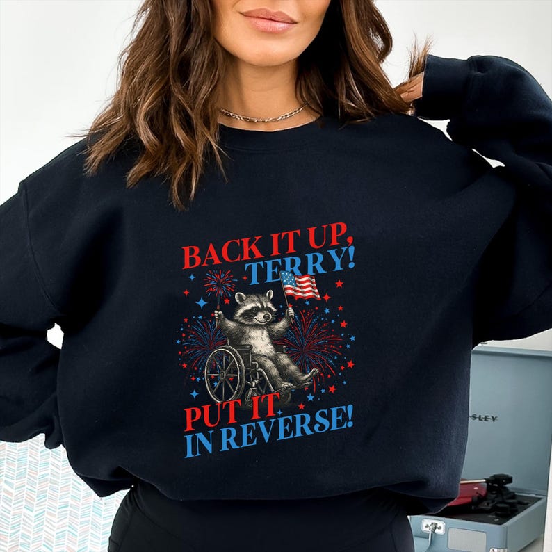 May include: Black sweatshirt with the text "BACK IT UP, TERRY! PUT IT IN REVERSE!" featuring a raccoon in a wheelchair holding an American flag, surrounded by red, white, and blue fireworks.