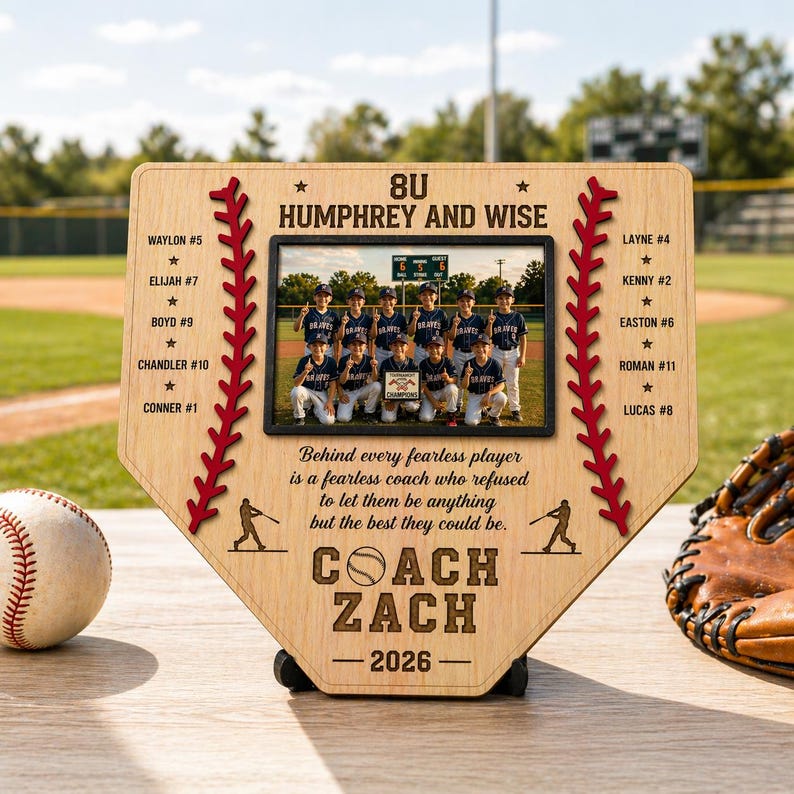 May include: A wooden baseball home plate-shaped plaque with a photo of a youth baseball team. The plaque has red stitching and text that reads "COACH ZACH 2026". A baseball and glove are next to the plaque.