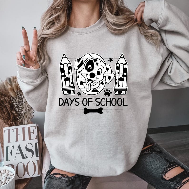May include: A gray sweatshirt with a black and white illustration of a dog with a tongue sticking out. The dog is surrounded by pencils and paw prints. The text "Days of School" is printed below the dog.