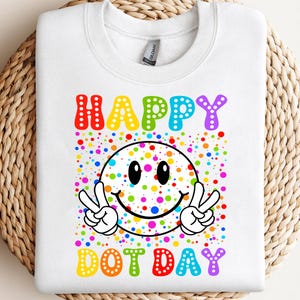 May include: White sweatshirt with a colorful graphic. The graphic features a smiley face with peace signs, surrounded by multi-colored dots. The words "HAPPY DOT DAY" are written in rainbow colors.