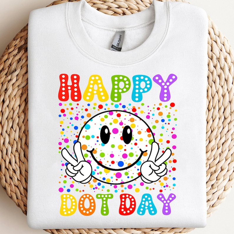 May include: White sweatshirt with a colorful graphic. The graphic features a smiley face with peace signs, surrounded by multi-colored dots. The words "HAPPY DOT DAY" are written in rainbow colors.