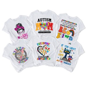 May include: Five white t-shirts with different designs featuring colorful graphics and text. The designs include a nurse with a stethoscope, a heart with puzzle pieces, a cat with sunglasses, a rainbow with the text "Be Kind", and a puzzle piece heart with the text "Autism Mom".