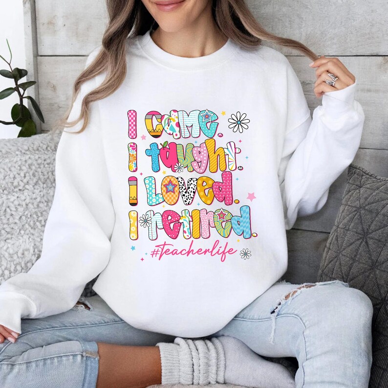 May include: White sweatshirt with the text "I came, I taught, I loved, I retired" in colorful, playful lettering. The design includes stars, flowers, and the hashtag #Teacherlife, making it a perfect gift for a retired teacher.