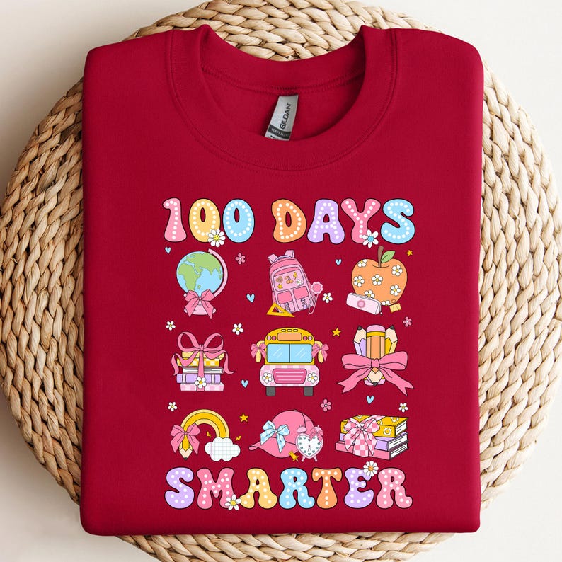 May include: A maroon sweatshirt with a colorful graphic celebrating 100 days of school. The design includes a globe, backpack, apple, school bus, and the word "SMARTER". The sweatshirt is made of a soft material.