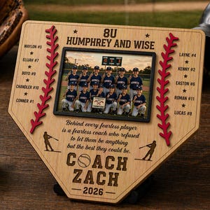 May include: A wooden baseball-themed plaque with a photo of a team, red stitching, and player names. The plaque reads "8U Humphrey and Wise" and "Coach Zach - 2026." A baseball and glove are visible.