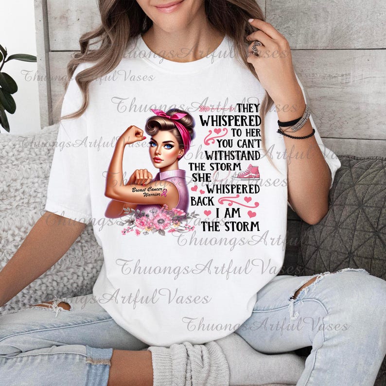 Puede incluir: Camiseta blanca con un gr&aacute;fico rosa y blanco de una mujer con un brazo fuerte, una cinta rosa y el texto "They whispered to her you can't withstand the storm she whispered back I am the storm".