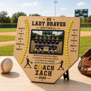May include: A wooden baseball home plate-shaped plaque featuring a team photo, team name, and player names. The plaque includes the text "8U Lady Braves Softball" and "Coach Zach - 2026". A baseball and glove are visible.