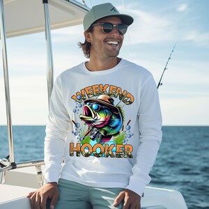 K&ouml;nnte beinhalten: Wei&szlig;er Langarm-Pullover mit einem Cartoon-Barsch, der eine Sonnenbrille und einen Hut tr&auml;gt. Der Text "Weekend Hooker" ist auf dem Pullover aufgedruckt.