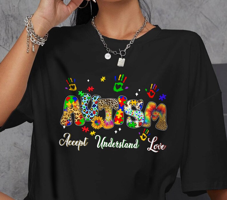 May include: Black t-shirt featuring a colourful graphic of the word "Autism" made up of jigsaw pieces, animal print, and tie-dye patterns. The text "Accept Understand Love" is below the graphic.