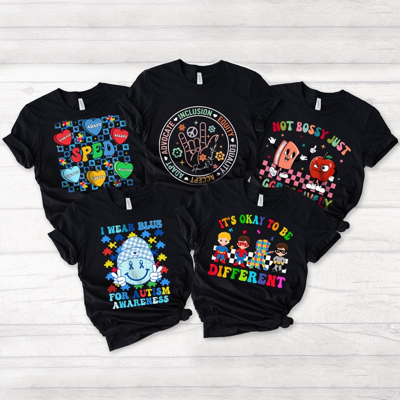May include: Five black t-shirts with different designs related to autism awareness. The designs include a puzzle piece heart with the word "SPED", a hand with the words "Advocate, Adapt, Accept, Inclusion, Equity, Equality", a cartoon apple and a slice of bread with the words "Not Bossy Just Goofy", a blue puzzle piece with a smiling face and the words "I Wear Blue For Autism Awareness", and four cartoon superheroes with the words "It's Okay To Be Different".