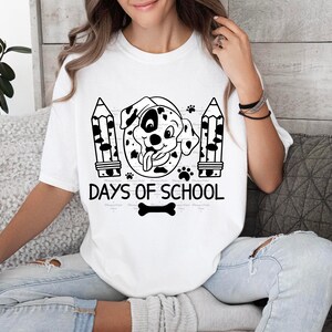 May include: White t-shirt with a black and white illustration of a Dalmatian dog wearing a graduation cap. The text "101 Days of School" is printed below the dog. A black and white bone is printed below the text.