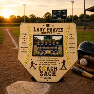 May include: A wooden softball team plaque in the shape of home plate. It features a team photo, player names, and the text "8U Lady Braves Softball." The plaque includes the coach's name, "Coach Zach," and the year "2026."