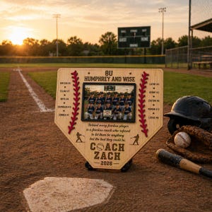 May include: A wooden baseball-shaped plaque with a team photo, names, and the text "COACH ZACH - 2026." The plaque has a baseball stitch design and is on a baseball field with a helmet, glove, ball, and bat.