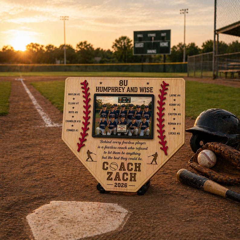 May include: A wooden baseball-shaped plaque with a team photo, names, and the text "COACH ZACH - 2026." The plaque has a baseball stitch design and is on a baseball field with a helmet, glove, ball, and bat.