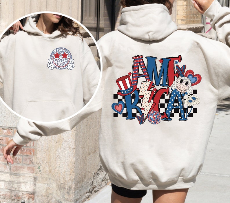May include: A white hoodie with a red, white, and blue "AMERICA" graphic on the back. The graphic includes a smiley face, stars, a lightning bolt, a checkered pattern, and a red, white, and blue top hat. The front of the hoodie has a white and blue smiley face with stars for eyes.