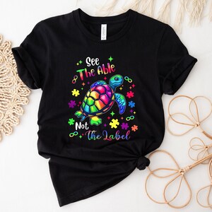 May include: Black t-shirt with a rainbow colored turtle and the text "See The Able Not The Label" with puzzle pieces and infinity symbols.