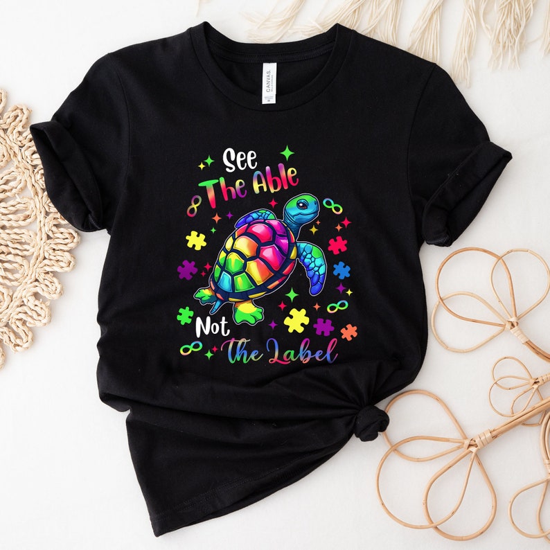 May include: Black t-shirt with a rainbow colored turtle and the text "See The Able Not The Label" with puzzle pieces and infinity symbols.