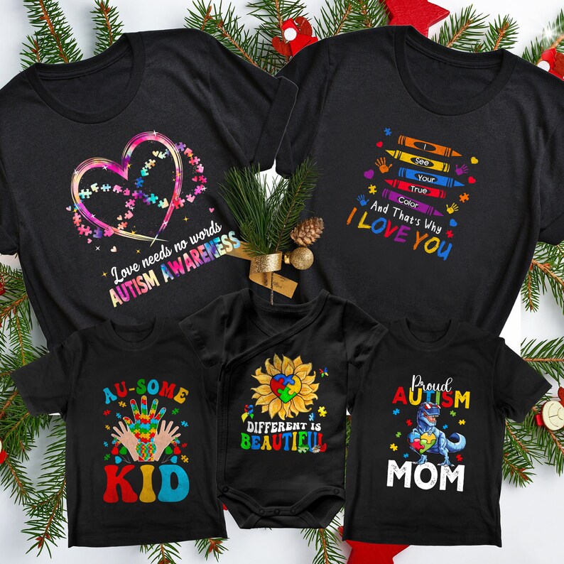 May include: Set of four black t-shirts with autism awareness designs. The shirts feature a heart made of jigsaw pieces, a sunflower with a jigsaw piece in the centre, a handprint with jigsaw pieces, and a dinosaur holding a jigsaw piece. The shirts also include the text "Love needs no words Autism Awareness", "Au-some Kid", "Different is Beautiful", and "Proud Autism Mom".