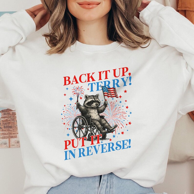 May include: White sweatshirt with a graphic of a raccoon in a wheelchair holding an American flag and fireworks. Text reads "BACK IT UP, TERRY! PUT IT IN REVERSE!" in red and blue.