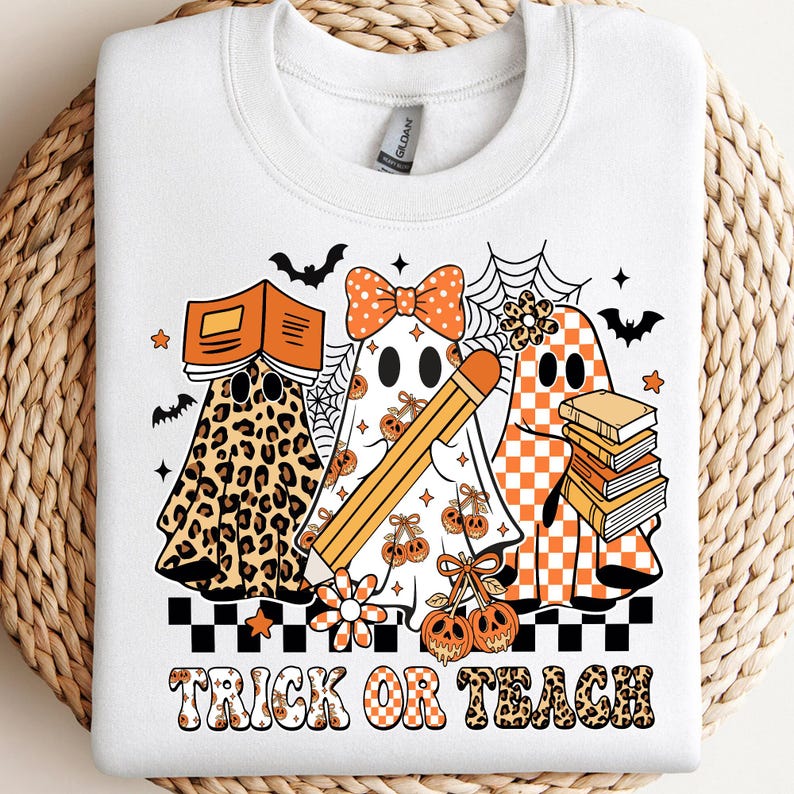May include: White sweatshirt with a Halloween-themed graphic. The design features three ghost characters, each with unique patterns and accessories, including books, a pencil, and a bow. The phrase "TRICK OR TEACH" is printed in a retro font.