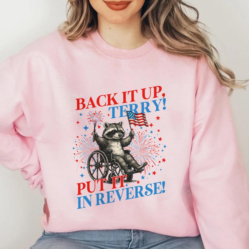 May include: Pink sweatshirt with the text "BACK IT UP, TERRY! PUT IT IN REVERSE!" featuring a raccoon in a wheelchair holding a sparkler and an American flag. The design includes fireworks and stars.