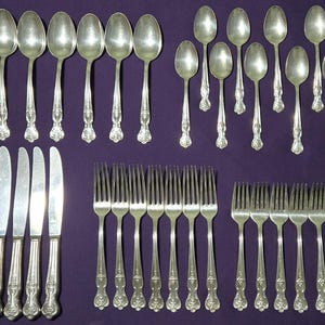 Puede incluir: Una gran colección de cubiertos de tono plateado que incluye ocho cuchillos de mesa con hojas lisas, ocho cucharas grandes, ocho cucharas pequeñas y dieciséis tenedores de varios tamaños. Cada pieza presenta un diseño de mango en relieve.