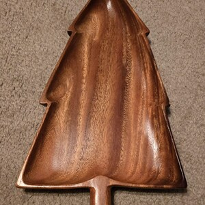 May include: A wooden Christmas tree-shaped serving dish. The dish is made of dark brown wood with a natural wood grain pattern.