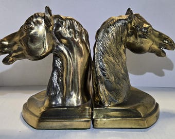 Puede incluir: Un par de sujetalibros antiguos de latón, cada uno esculpido con la forma de una cabeza de caballo. Los sujetalibros tienen un acabado metálico, que resalta la melena y los rasgos faciales del caballo. La base rectangular proporciona estabilidad.