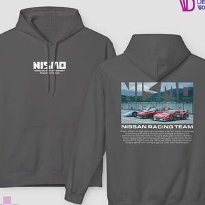 Op de afbeelding: Donkergrijze hoodie met de tekst "NISMO" en "NISSAN MOTORSPORT RACE TEAM" op de voorkant. De achterkant toont een afbeelding van Nissan-raceauto's met de tekst "NISSAN RACING TEAM".