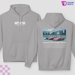 May include: A light gray hoodie with a front and back design. The front features the word "NISMO" in white. The back displays a graphic of race cars with the text "NISSAN RACING TEAM" and additional text below. The hoodie has a drawstring hood.