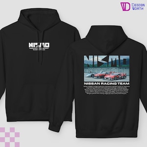 May include: Black hoodie with a white NISMO logo on the front and a graphic of racing cars on the back. The back graphic includes the text "NISSAN RACING TEAM". The hoodie has a hood and a front pocket.