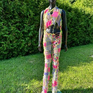 May include: A patchwork jumpsuit with a pink, purple, and white color scheme. The jumpsuit has a sleeveless top and long pants with a lace-up detail on the front. The jumpsuit is made of a sheer fabric and has a distressed look.