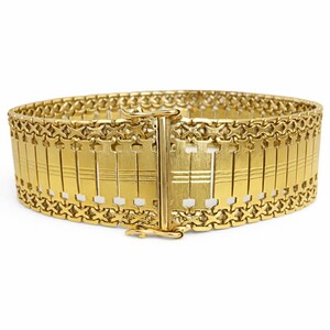 May include: A wide, gold-colored bracelet with a rectangular design. The bracelet features a series of vertical bars connected by a decorative chain. The clasp is centered and secures the bracelet. The jewelry is set against a white background.