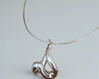 Puede incluir: Collar plateado con un colgante abstracto y fluido. El colgante presenta un diseño en bucle con un acabado pulido, suspendido de una fina cadena tipo gargantilla plateada. El fondo es de color neutro.