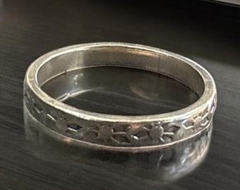 May include: A silver ring with a repeating floral pattern around the band. The ring is made of a shiny metal and reflects the surrounding environment. The ring is a simple band style.