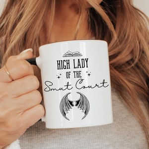 May include: White ceramic mug with a black design that reads "High Lady of the Smat Court" with a pair of wings underneath the text.
