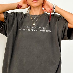 May include: A dark gray oversized t-shirt with the text "I dust my shelves but my books are still dirty" printed on the front.
