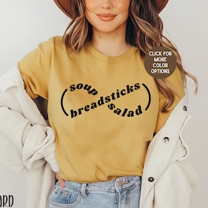 May include: A mustard yellow t-shirt with black text that reads "(soup breadsticks) salad".