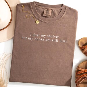 May include: A brown t-shirt with the text "i dust my shelves but my books are still dirty" printed in white.