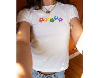 May include: White t-shirt with a rainbow of colorful flower designs on the front.